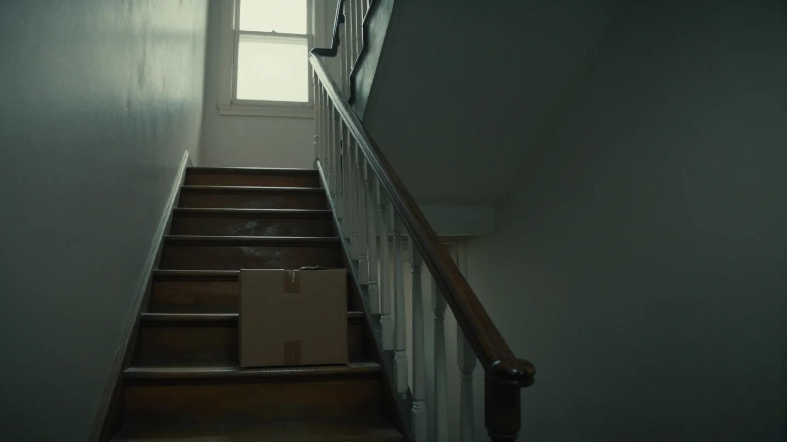 Looking up a narrow apartment stairwell with a single cardboard box on a middle step